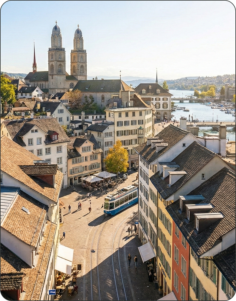 Ein blaues Tram fährt durch eine von bunten Gebäuden gesäumte Kopfsteinpflasterstraße in Zürich, mit der Großmünsterkirche und dem Fluss im Hintergrund.